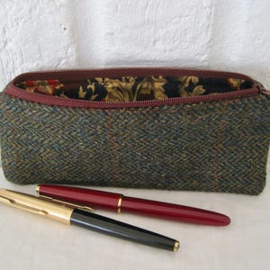 May include: A green tweed pencil case with a red zip and floral lining. Two pens, one gold and black, the other red, are in front of the case. The case is approximately 20 cm long.