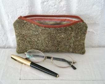 May include: A tweed pouch with a brown zip and a patterned interior, alongside a pair of spectacles and a gold and black pen. The pouch is open, showing the colourful lining.