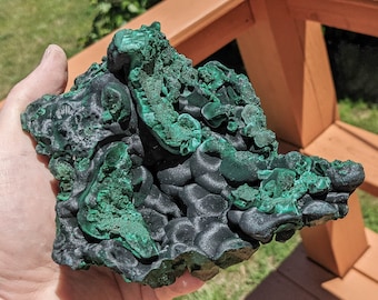 May include: A large, green malachite rock with a rough, textured surface. The rock has a dark green color with lighter green accents.