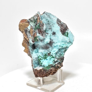Peut inclure: Un spécimen minéral bleu et vert de forme irrégulière et rugueuse. Le spécimen est monté sur un support en acrylique transparent.