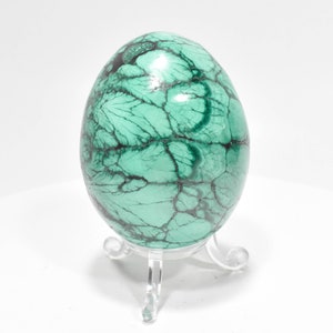 May include: A green malachite egg with black veins, displayed on a clear plastic stand.