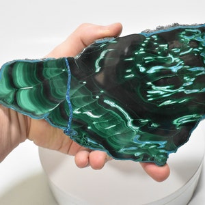 May include: A large, polished slab of malachite with a green and blue color pattern. The malachite has a smooth, shiny surface and is a beautiful example of this popular gemstone.
