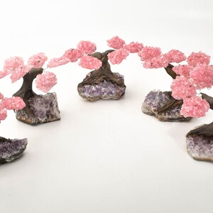 May include: Four pink rose quartz crystal trees on amethyst bases. The trees are arranged in a semi-circle, with the branches of the trees touching.