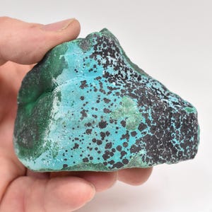 May include: A large, irregularly shaped piece of malachite with a green and blue colour. The malachite has black spots and streaks throughout.