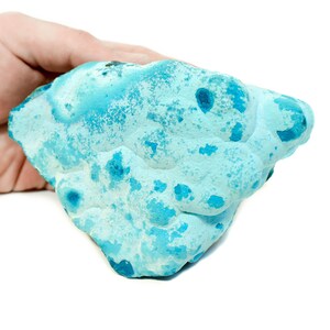 May include: A large, blue, irregularly shaped piece of turquoise gemstone. The gemstone has a rough, textured surface with a variety of blue hues.