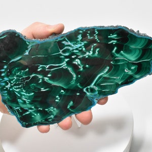 May include: A large, green malachite slab with a swirling, banded pattern. The slab has a smooth, polished surface and a rough, natural edge.