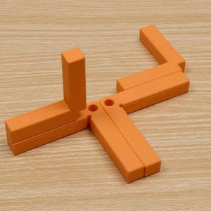May include: An orange, geometric puzzle toy composed of several rectangular pieces connected by hinges. The pieces are arranged in a star-like configuration on a light wood-grain surface. The toy's design suggests a focus on spatial reasoning and problem-solving.