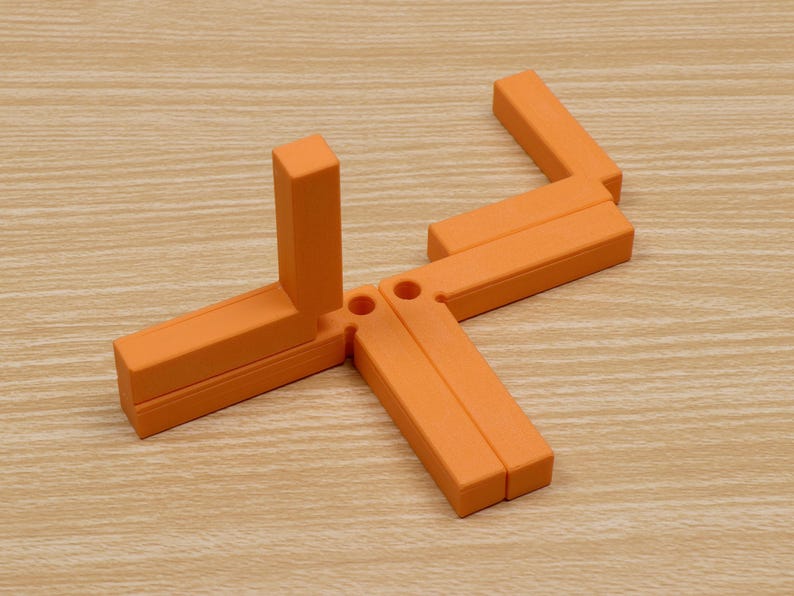 May include: An orange, geometric puzzle toy composed of several rectangular pieces connected by hinges. The pieces are arranged in a star-like configuration on a light wood-grain surface. The toy's design suggests a focus on spatial reasoning and problem-solving.