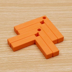 May include: Orange, L-shaped trivets arranged in an arrow formation. Each trivet has a hole in the corner. The trivets are made of a solid material and are on a light wood-grain surface. The trivets are designed to protect surfaces from hot items.