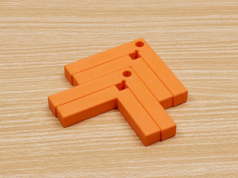 May include: Orange, L-shaped trivets arranged in an arrow formation. Each trivet has a hole in the corner. The trivets are made of a solid material and are on a light wood-grain surface. The trivets are designed to protect surfaces from hot items.