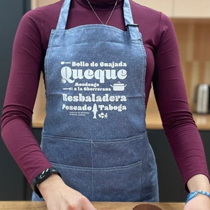 以下が含まれることがあります： 白い文字で「Bollo de Cuajada Queque Mondongo a la Chorrerana Resbaladera Pescado Taboga Platos del Recetario de Muestra, Carioca」と書かれた青いデニムのエプロン。