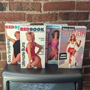 May include: Three VHS tapes for workout videos. The tapes are titled "Redbook Ultimate Buns", "Denise Austin Super Stomach", and "Denise Austin Trim Walk". The tapes feature women in workout attire.