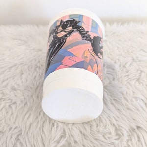 May include: White plastic cup with a colorful image of Catwoman from the Batman movie. The image features Catwoman in a black leather suit with a whip and a cityscape background.