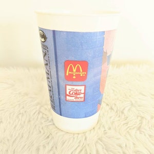 May include: White plastic cup with a blue and pink Batman Returns design. The cup features the McDonald's logo and a Diet Coke logo.