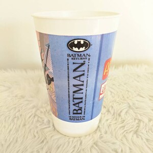 May include: A white plastic cup with a blue and red Batman Returns design. The cup features the Batman logo and the text "Batman Returns" and "Le Retour de Batman".