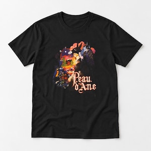May include: A black short-sleeved t-shirt featuring a colourful graphic print of a person wearing a donkey headpiece, surrounded by flowers and a sunset landscape, with the text Peau d'Ane printed in a stylised font at the bottom.