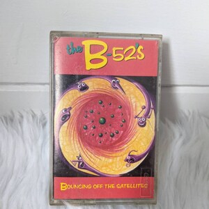 May include: A cassette tape with a red, yellow and purple design. The tape is titled "the B-52's" and "BOUNCING OFF THE SATELLITES".