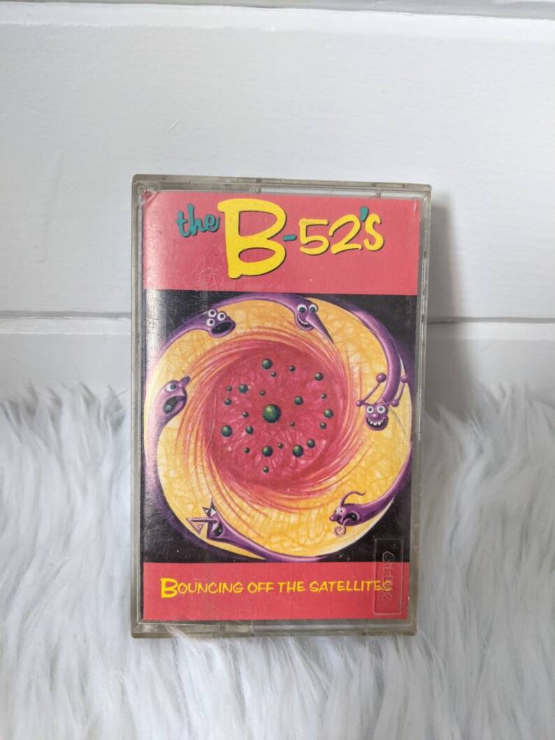May include: A cassette tape with a red, yellow and purple design. The tape is titled "the B-52's" and "BOUNCING OFF THE SATELLITES".