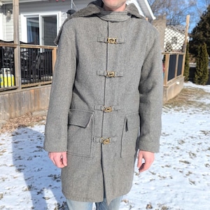 May include: A gray wool coat with a hood and a brown fur lining. The coat has a high collar and five gold toggle closures.