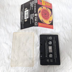 May include: A black cassette tape case with the title "B-52's Bouncing Off The Satellites" printed on the front. The case has a colourful image of a swirling vortex with black, red, yellow, and orange colours.