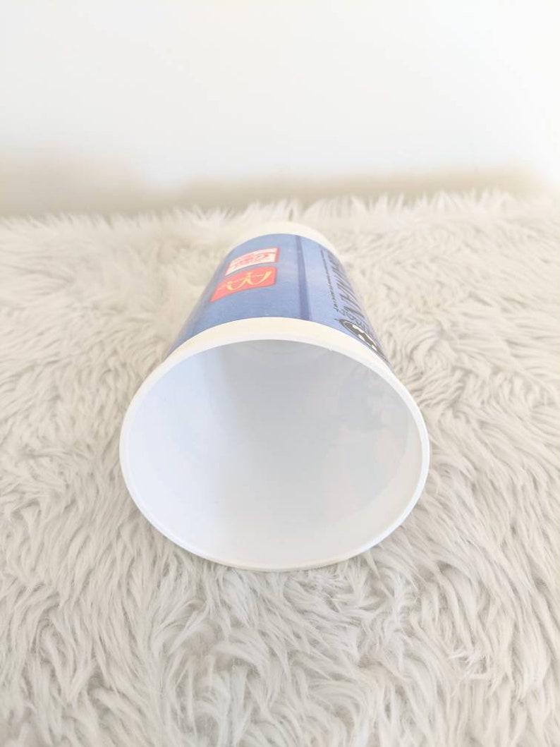 May include: White disposable cup with a blue and red design. The cup has the McDonald's logo and the text "McCafe" printed on it.