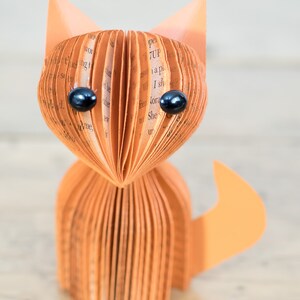 May include: A brown paper fox sculpture with black eyes. The fox is made from folded pages of a book.