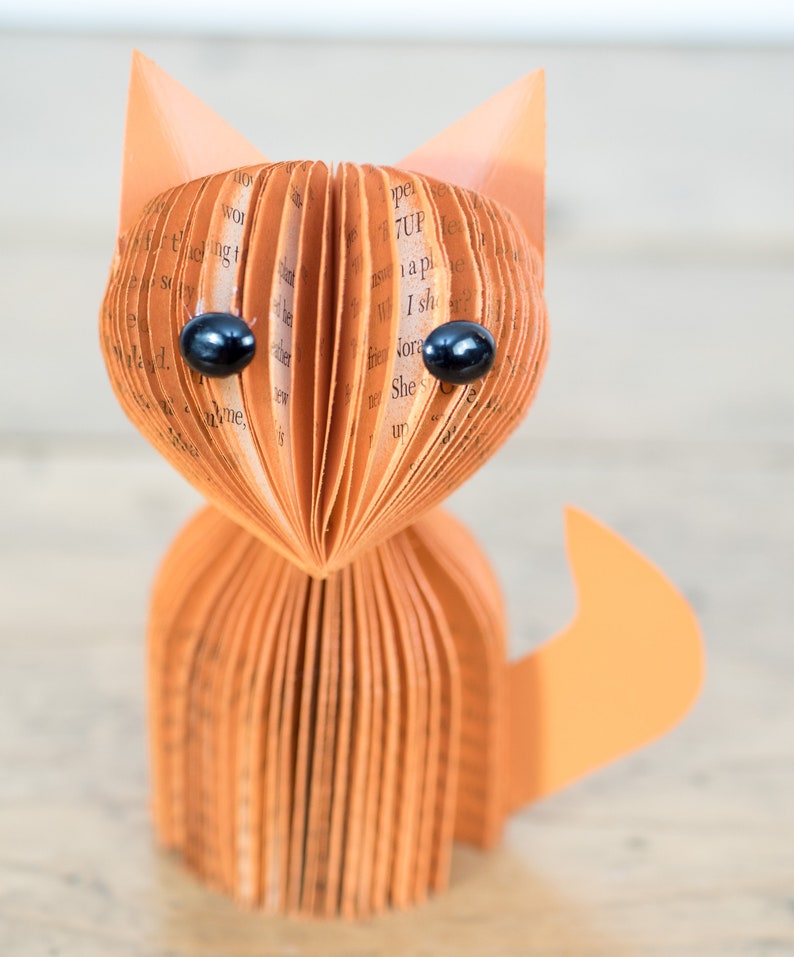 May include: A brown paper fox sculpture with black eyes. The fox is made from folded pages of a book.
