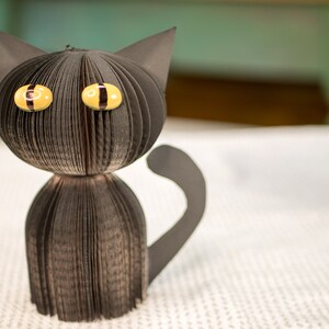 May include: A black paper cat with yellow eyes. The cat is made from folded paper and has a three-dimensional appearance.
