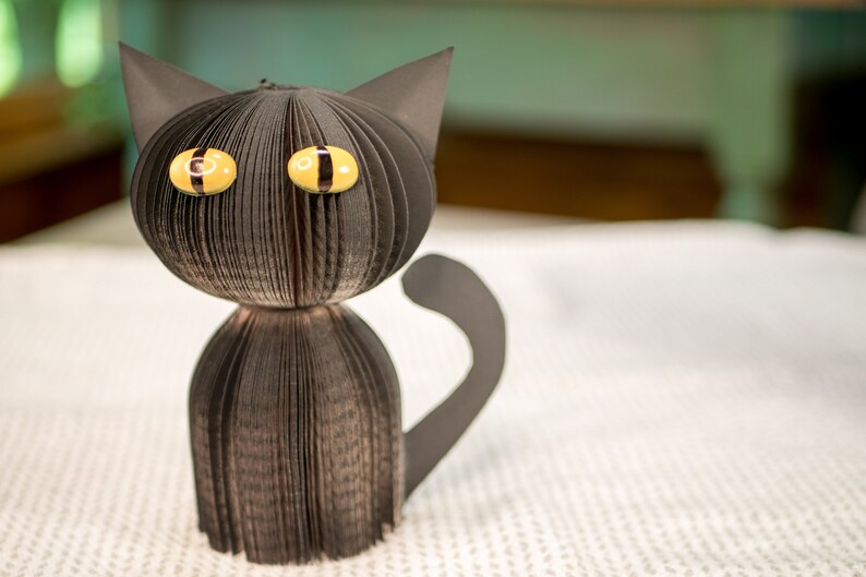 May include: A black paper cat with yellow eyes. The cat is made from folded paper and has a three-dimensional appearance.