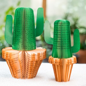 Op de afbeelding: Twee groene papieren cactus-boekenleggers gemaakt van gevouwen boekpagina's. De boekenleggers staan op een wit oppervlak.