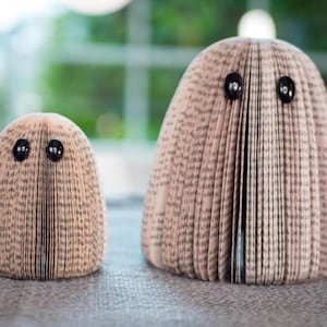 May include: Two book folding sculptures, one large and one small, are made from pages of a book and have black button eyes.