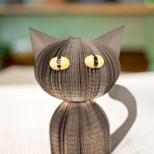 May include: A black paper cat with yellow eyes. The cat is made from folded paper and has a three-dimensional appearance.