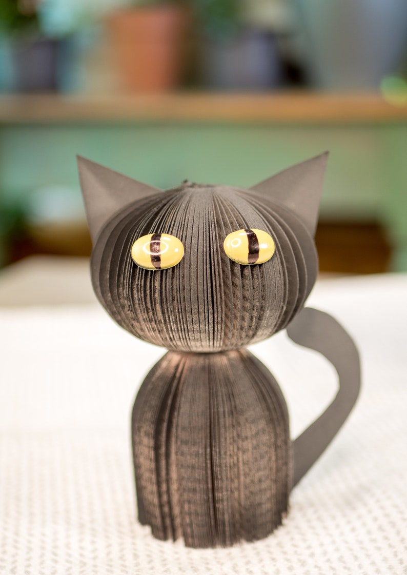 May include: A black paper cat with yellow eyes. The cat is made from folded paper and has a three-dimensional appearance.