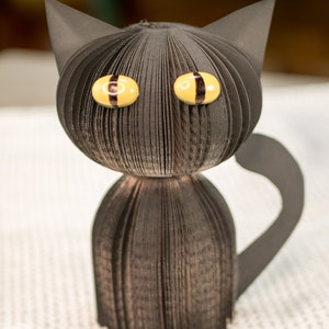 May include: A black paper cat with yellow eyes and a black tail. The cat is made from folded paper and has a 3D effect.