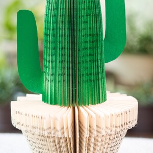 Op de afbeelding: Een groene papieren cactus gemaakt van de pagina's van een boek. De cactus staat op een boek met de pagina's waaiervormig uitgespreid.