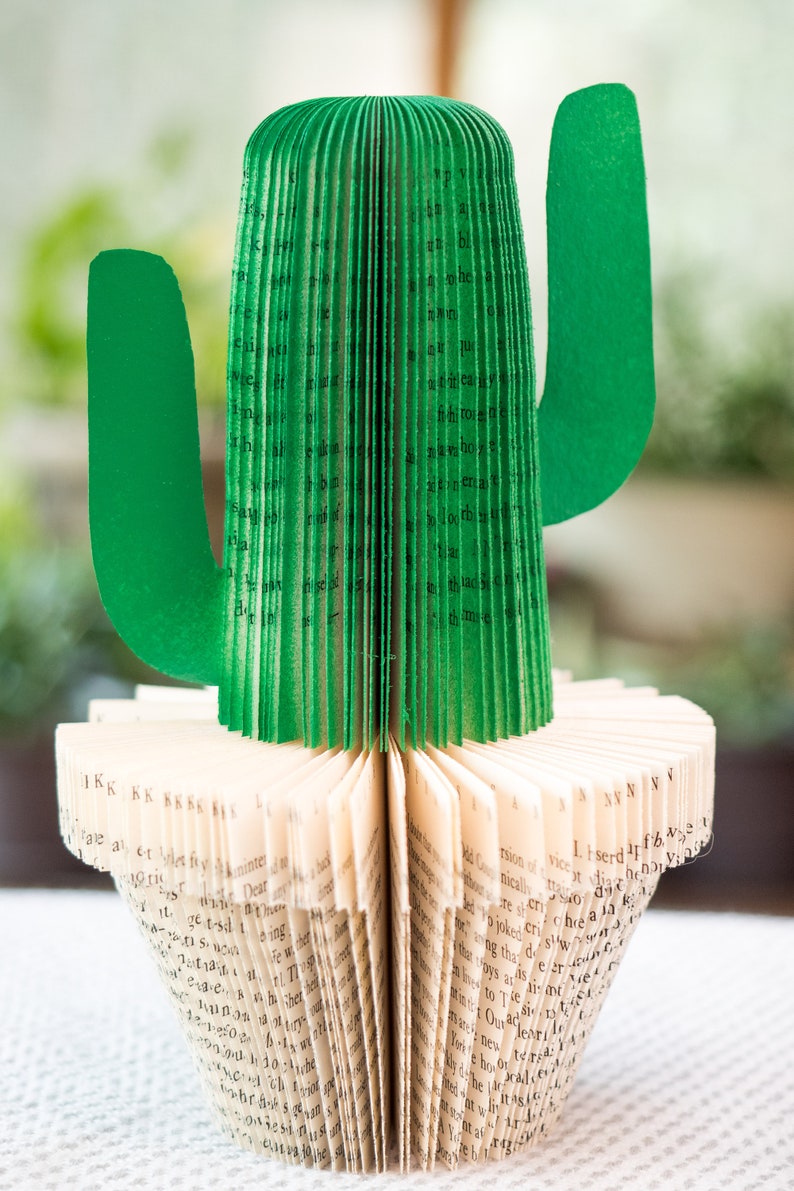 Op de afbeelding: Een groene papieren cactus gemaakt van de pagina's van een boek. De cactus staat op een boek met de pagina's waaiervormig uitgespreid.