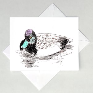 May include: A greeting card featuring a detailed pen and ink illustration of a duck swimming in water. The duck has a purple head, black body, and a turquoise beak. The card is white and is placed on top of a white envelope.
