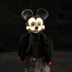 Puede incluir: Un t&iacute;tere vintage de Mickey Mouse en blanco y negro con un cuerpo de fieltro negro y manos de fieltro rojo. El t&iacute;tere tiene una cabeza grande con orejas negras y una cara blanca con ojos negros y una nariz negra.