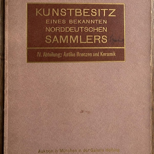 Puede incluir: Un catálogo de subastas antiguo con una cubierta de color rosa polvoriento y un recuadro rectangular marrón oscuro. El texto dice KUNSTBESITZ EINES BEKANNTEN NORDDEUTSCHEN SAMMLERS, IV. Abteilung: Antike Bronzen und Keramik, y Auktion in München in der Galerie Helbing am 22. Februar 1910.