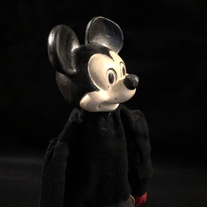Puede incluir: Un mu&ntilde;eco vintage de Mickey Mouse en blanco y negro con un su&eacute;ter negro. El mu&ntilde;eco tiene la cara blanca con ojos negros y una nariz negra.