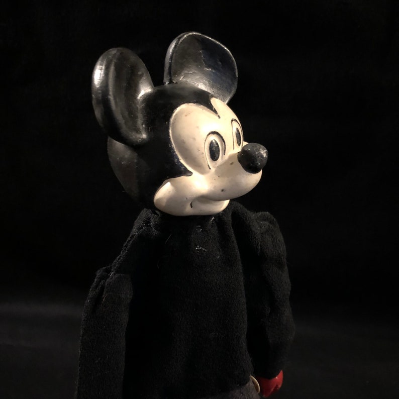 Puede incluir: Un mu&ntilde;eco vintage de Mickey Mouse en blanco y negro con un su&eacute;ter negro. El mu&ntilde;eco tiene la cara blanca con ojos negros y una nariz negra.