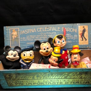 Puede incluir: Una caja de madera vintage con una etiqueta azul y blanca que dice "Pastina Celestiale Baroni - Glutinata -" y presenta una imagen de dibujos animados de un beb&eacute; en una trona. La caja contiene una colecci&oacute;n de juguetes de personajes vintage, incluyendo Mickey Mouse, Donald Duck y otros personajes.