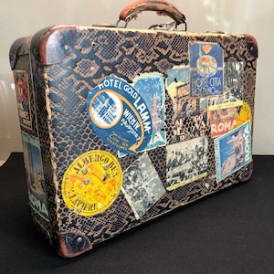 Estuche de viaje de cartón efecto pitón, etiquetas con ubicaciones turísticas y detalles de cuero, principios del siglo XX, Italia.