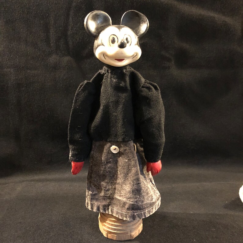 Puede incluir: Un t&iacute;tere de mano vintage de Mickey Mouse con un cuerpo de fieltro negro, guantes de fieltro rojo y una cabeza de porcelana negra y blanca. El t&iacute;tere est&aacute; de pie sobre una base de madera.