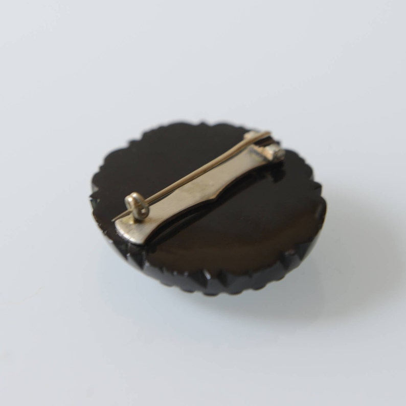 May include: Black jet brooch with a silver tone pin and catch on the back.
