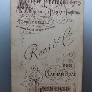 May include: A vintage business card with brown text on a white background. The text reads 'Artiste Photographers Miniature & Portrait Painters Prize Medal Awarded South London Exhibition Rees & Co 298 Clapham Road London S.W. N° 101164'
