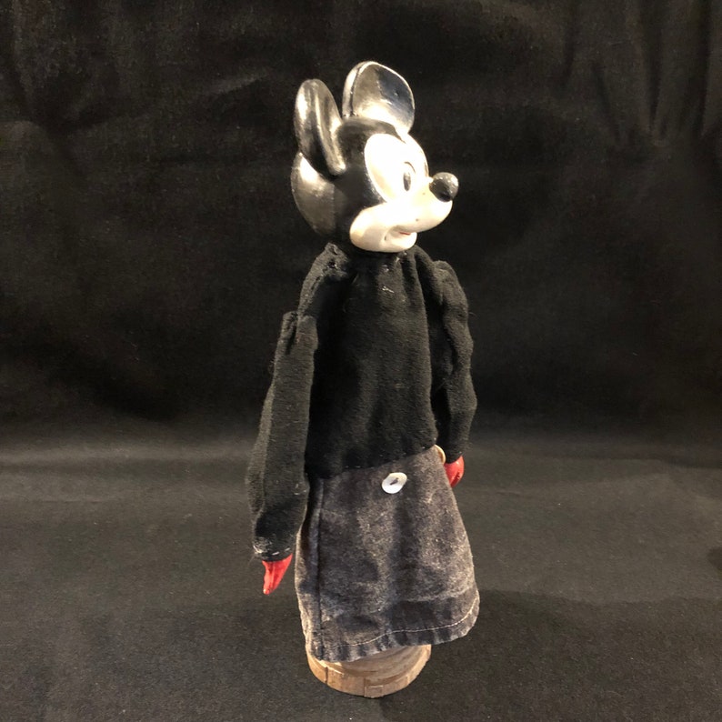Puede incluir: Un t&iacute;tere vintage de Mickey Mouse en blanco y negro con guantes rojos y una camisa negra. El t&iacute;tere lleva una falda vaquera con un bot&oacute;n en la espalda. El t&iacute;tere est&aacute; de pie sobre una base de madera.