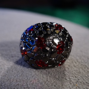 May include: A black ring with a textured surface and red gemstones.