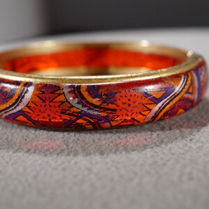 May include: A gold bangle bracelet with a red, orange, purple, and white geometric pattern.