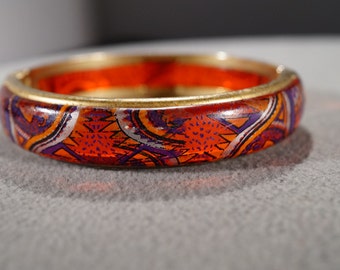 May include: A gold bangle bracelet with a red, orange, purple, and white geometric pattern.
